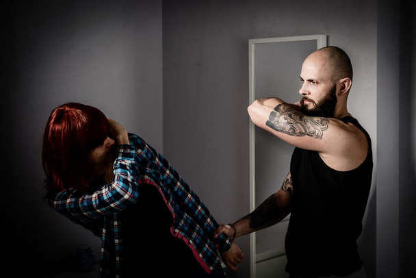 Мускулистый татуированный мужчина бьет свою рыжую жену
.  - Фото, изображение