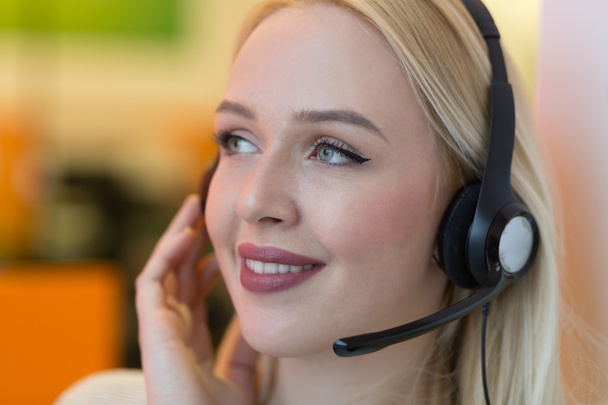 lächelnde junge Geschäftsfrau, die ein Headset trägt und Anrufe entgegennimmt - Foto, Bild