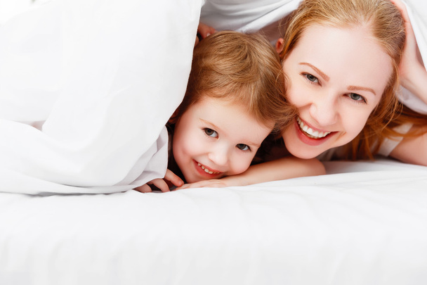 happy family mother and child playing and laughing in bed  - Фото, изображение