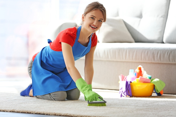 Νεαρή γυναίκα καθαρίζει το χαλί στην αίθουσα - Φωτογραφία, εικόνα