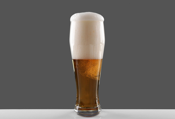 Glass of draft lager beer with thick froth on grey background - Photo, Image