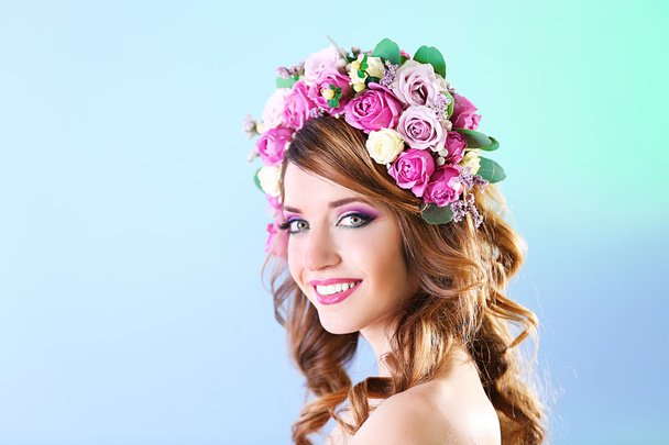 Beautiful young woman wearing floral headband on a blue background - Фото, зображення