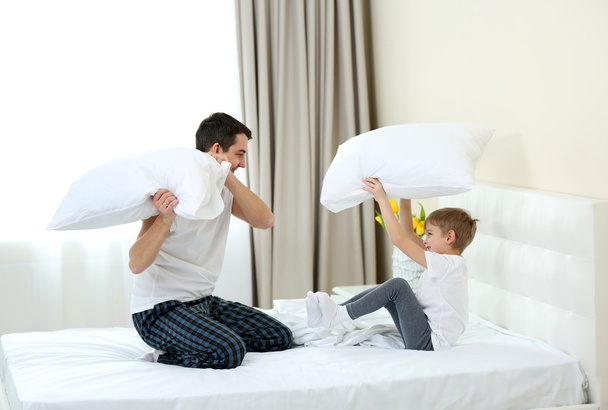 Παιχνιδιάρικο πατέρα και γιου που αγωνίζονται με μαξιλάρια στο κρεβάτι στο σπίτι - Φωτογραφία, εικόνα