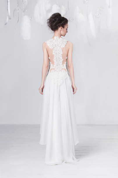 Tall and slim young bride in a luxurious lace wedding dress. She stands with her back to the viewer. - Фото, изображение