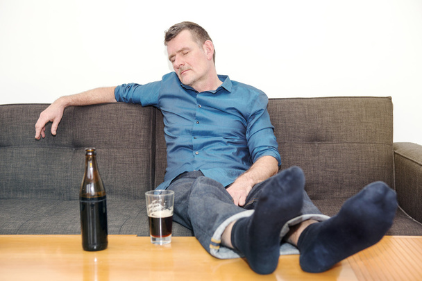 man sleeping on couch with bottle of beer on table - Fotoğraf, Görsel
