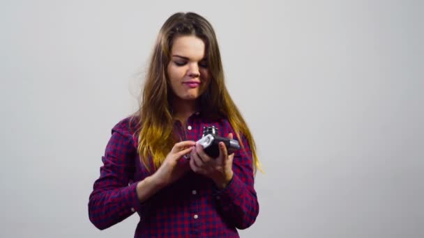young girl trying to understand old film camera in front of white background - Footage, Video