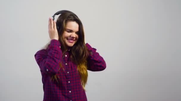 Молодая девушка слушать музыку с наушниками и танцы перед белой стеной
 - Кадры, видео
