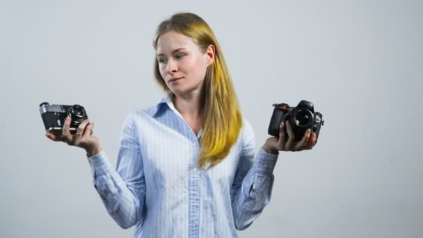 girl making a choice holding an old camera in one hand and new one in another - Footage, Video