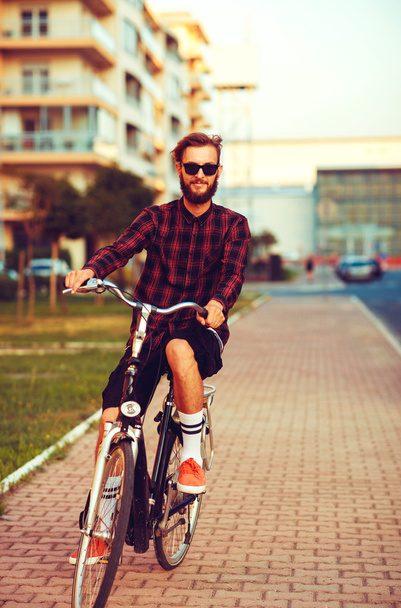 Stylish man in sunglasses riding a bike on city street - Photo, image