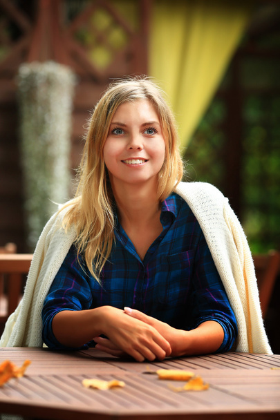 Ein Mädchen sitzt an einem Holztisch in einem Café. lächelt. Alter 20 Jahre - Foto, Bild