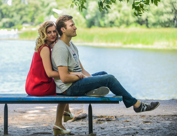 Young and happy couple sitting on the bench hugging. River background - Photo, Image