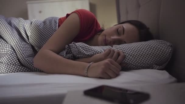 Schöne Brünette wacht in einem Bett auf und beginnt, ihr mobiles Gerät zu benutzen. - Filmmaterial, Video