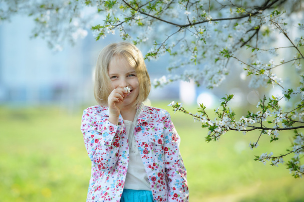 Beautiful happy little girl  enjoying smell in a flowering sprin - Фото, зображення