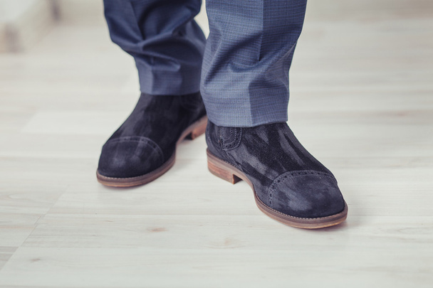 Benen van de mens in zwart suède laarzen permanent op het parket - Foto, afbeelding