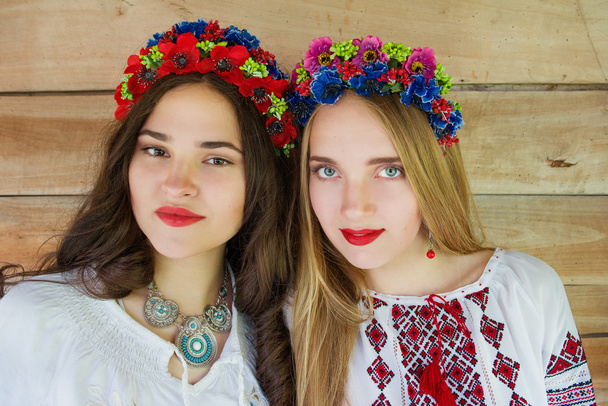 Dos chicas hermosas jóvenes con el pelo largo en blusas ucranianas y en una corona de flores en la aldea étnica al aire libre Pirogovo en Kiev Ucrania
 - Foto, Imagen