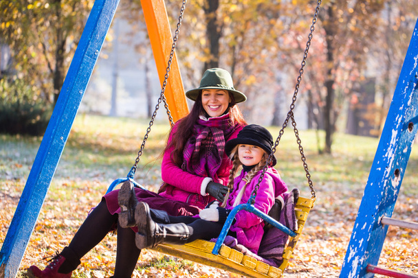 幸せな母と娘は、秋の公園のブランコに乗る。秋の公園で母と娘 - 写真・画像