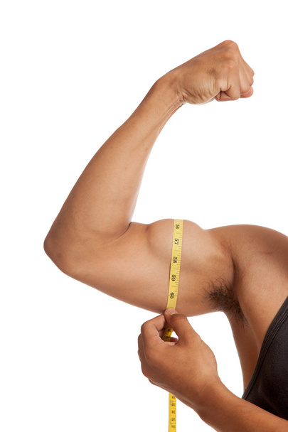 Muscular Asian man's arm flexing biceps with measuring tape - Photo, image
