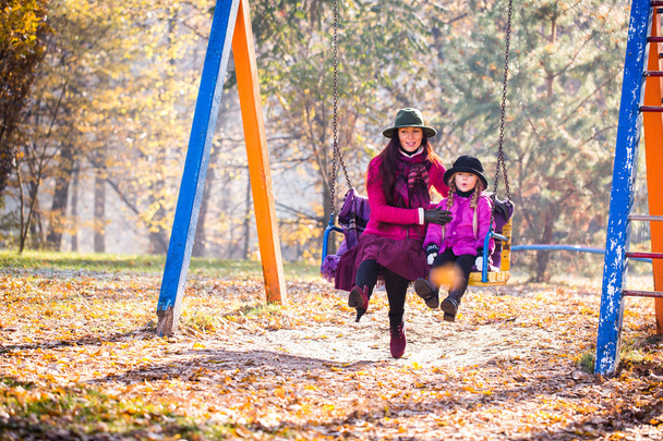 mutlu anne ve kızı sonbahar parkta bir salıncak üzerinde binmek. Anne ve kızı sonbahar parkta - Fotoğraf, Görsel