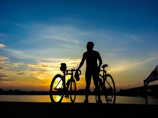 Polkupyöräilijä seisoo joella katsomassa auringonvaloa ja rentoutua
 - Valokuva, kuva