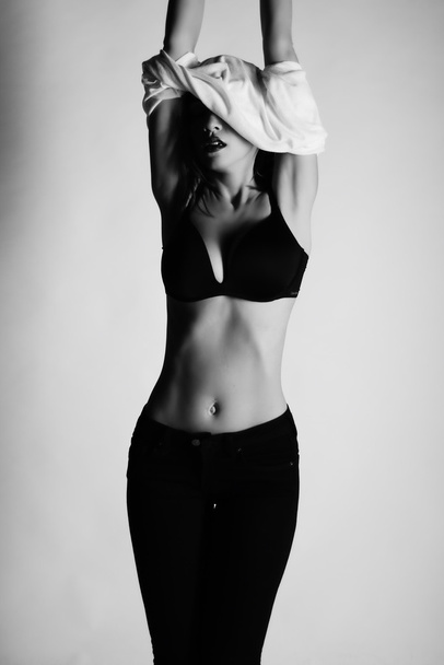 Siyah ve beyaz fotoğraf stüdyosunda poz güzel esmer kadın modeli. Kot pantolon, bra, t-shirt giyiyor - Fotoğraf, Görsel