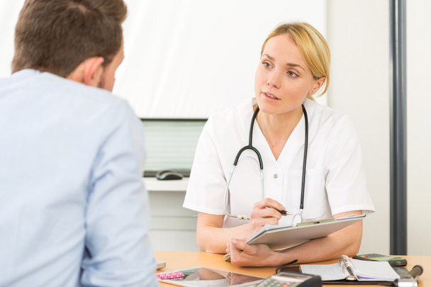 Young attractive woman doctor taking notes while patient speak - Foto, imagen