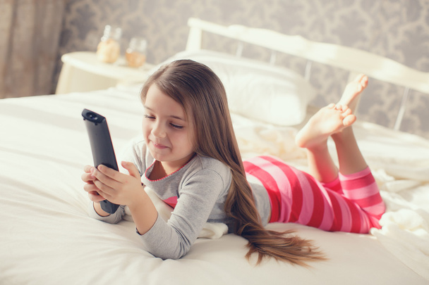 Little girl lying in bed with a remote control TV - Foto, afbeelding
