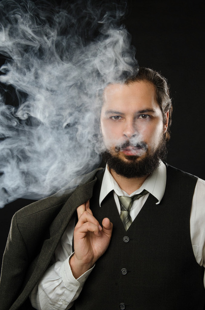 well-dressed man smoking electronic cigarette on black background - Foto, afbeelding
