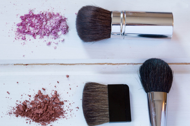women's accessories cosmetics. Makeup brushes and crushed eyeshadow on wooden background  - Photo, Image