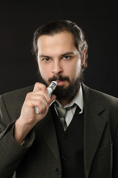 well-dressed man smoking electronic cigarette on black background - 写真・画像