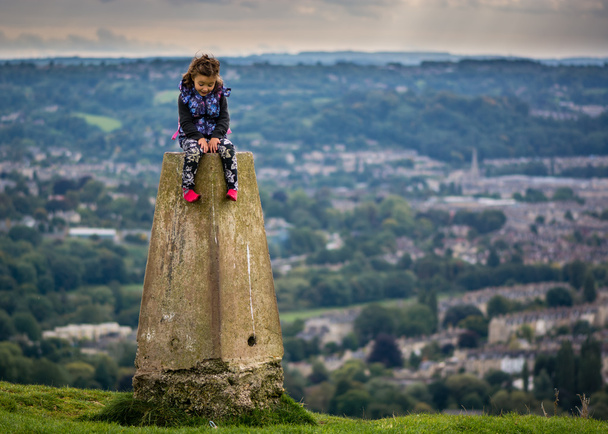 Young girl sitting on triangulation point on Little Solsbury Hill, overlooking the World Heritage City of Bath, Somerset, UK - Photo, Image