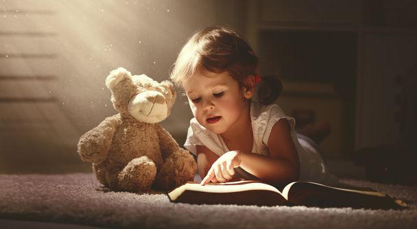 дитяча маленька дівчинка читає чарівну книгу в темному будинку
  - Фото, зображення