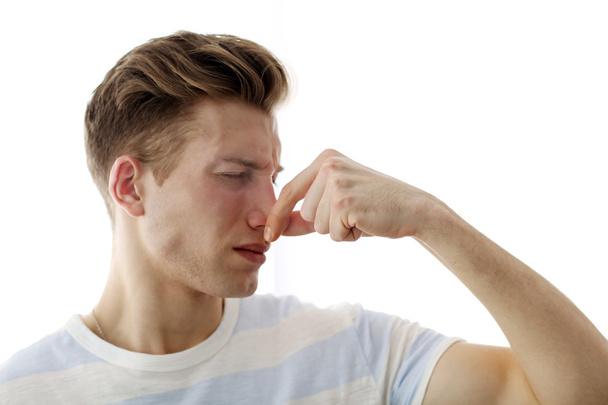 Young blonde man pinching his nose because of the stench, isolated on white - 写真・画像