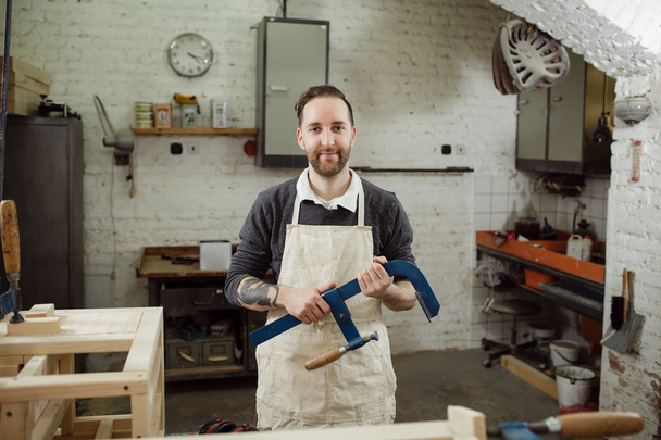 carpintero está mirando y sosteniendo una abrazadera azul
 - Foto, Imagen
