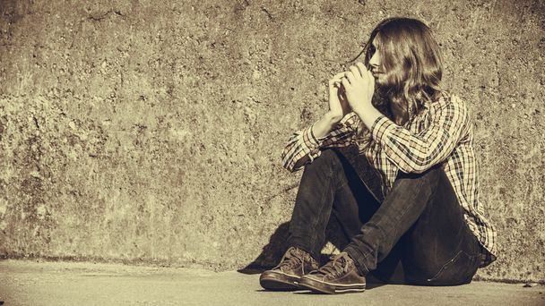 Man long haired sitting alone sad on grunge wall - Foto, afbeelding
