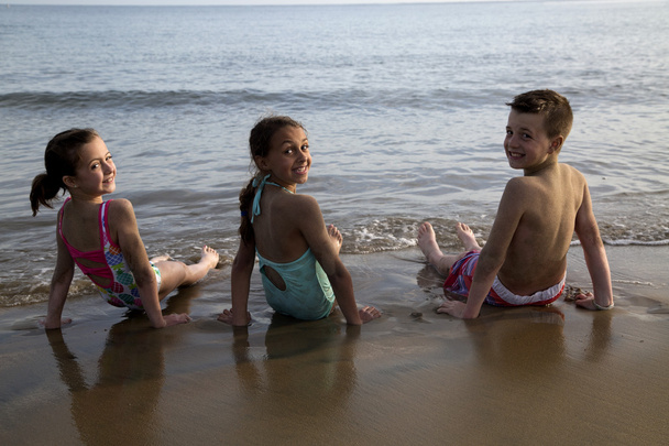 Three cute preteen children sitting in the water on the beach - Foto, afbeelding