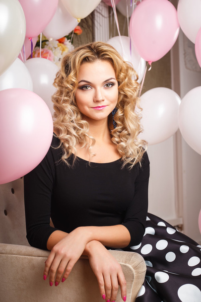 Beautiful curly young woman in a room with many pink and white air balloons. Beauty fashion portrait - Фото, изображение