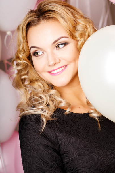 Close-up portrait of beautiful curly young woman in a room with many pink and white air balloons and flowers. Beauty fashion portrait - Photo, image