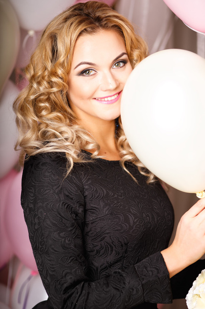 Close-up portrait of beautiful curly young woman in a room with many pink and white air balloons and flowers. Beauty fashion portrait - Foto, immagini