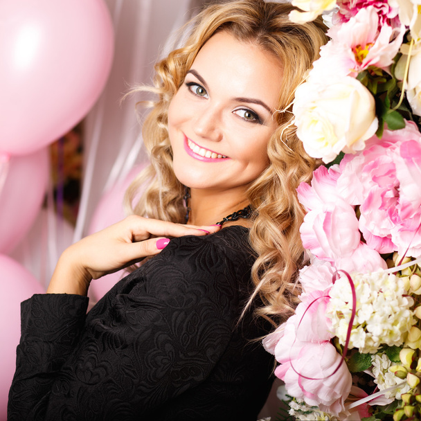 Close-up portrait of beautiful curly young woman in a room with many pink and white air balloons and flowers. Beauty fashion portrait - Zdjęcie, obraz