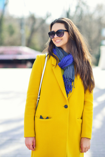 Young smiling brunette woman in a yellow coat and sunglasses, Sp - Foto, Imagem
