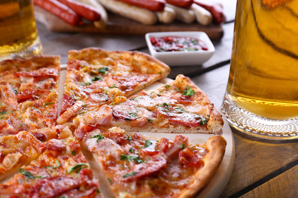Sliced pizza and glass of beer on wooden table, close up - Fotó, kép