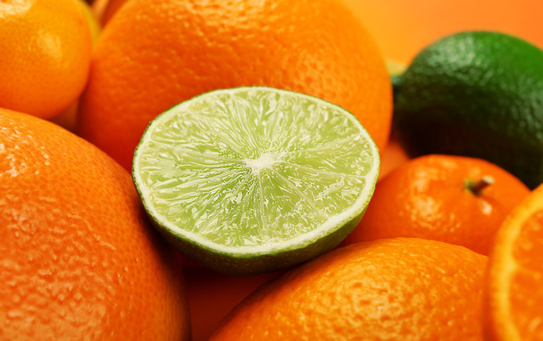 A heap of mixed citrus fruit with half of lime on top, close up - Fotografie, Obrázek
