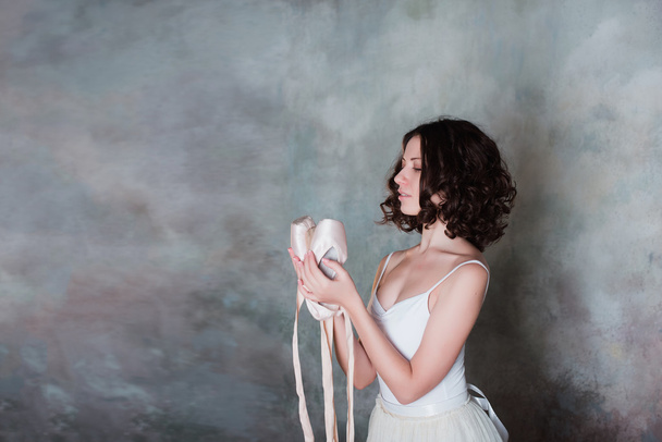 Portrait of a beautiful young ballerina holding hands pointe shoes for dance - Foto, Imagen