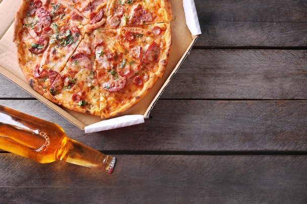 Tasty pizza in carton and bottle of beer are on wooden table, close up - Foto, Imagen