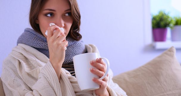 Portrait of a sick woman blowing her nose while sitting on the sofa - Foto, Imagem