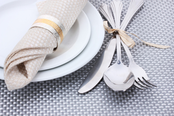 White empty plates with fork, spoon and knife tied with a ribbon on a grey tablecloth - 写真・画像