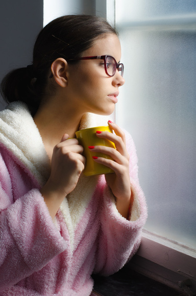 Красива дівчина в окулярах п'є ранкову каву перед вікном
 - Фото, зображення