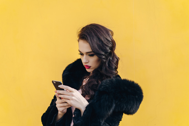 Beautiful girl with the phone on a yellow background - Valokuva, kuva