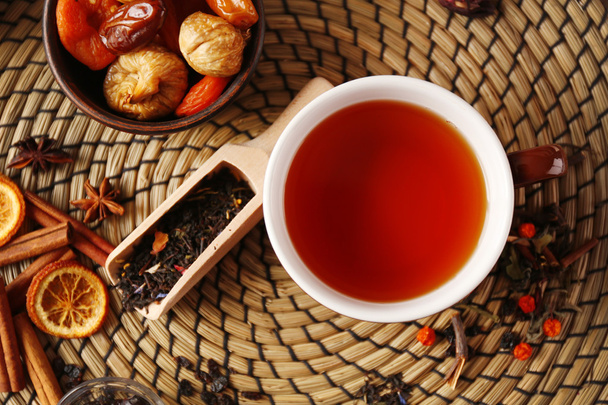 Cup of tea with spices and dried fruits on wicker tray, top view - 写真・画像