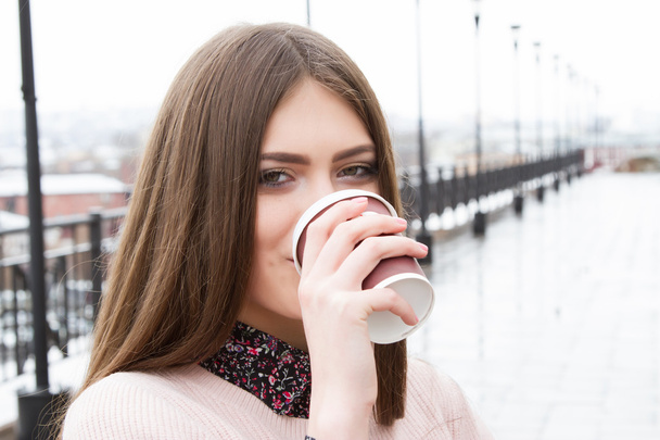 Молода дівчина п'є каву на відкритому повітрі в негоду
 - Фото, зображення